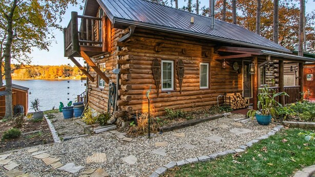 Una baita di legno con un balcone, un vialetto in pietra e vista su un lago.