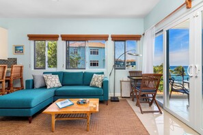 A living room with a teal sofa, wooden coffee table, and a view of the sea through large windows. - Blue Serenity Oceanfront Penthouse (Tower Isle)