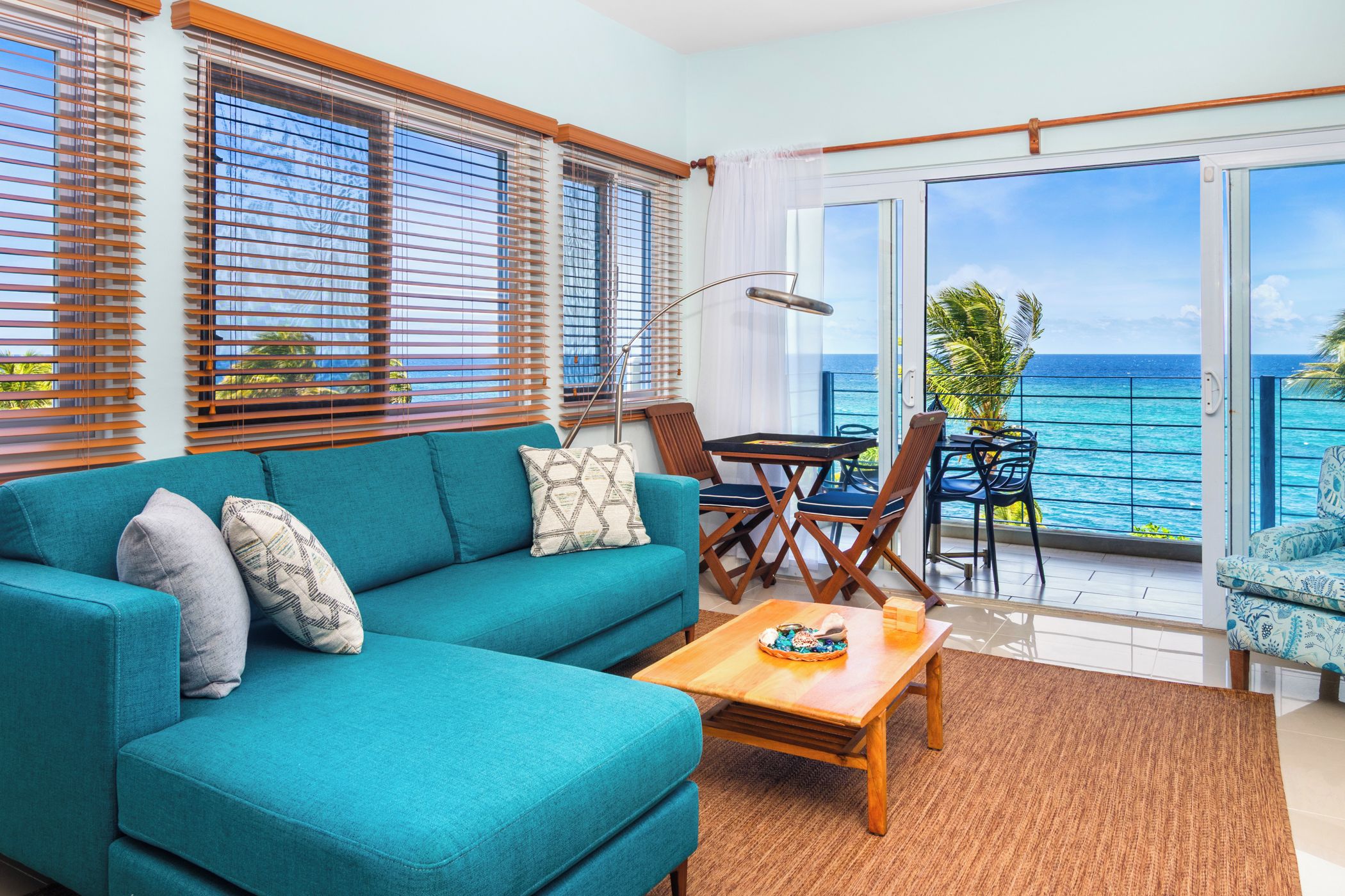 A living room with a teal sofa, wooden coffee table, and a view of the ocean through large windows.