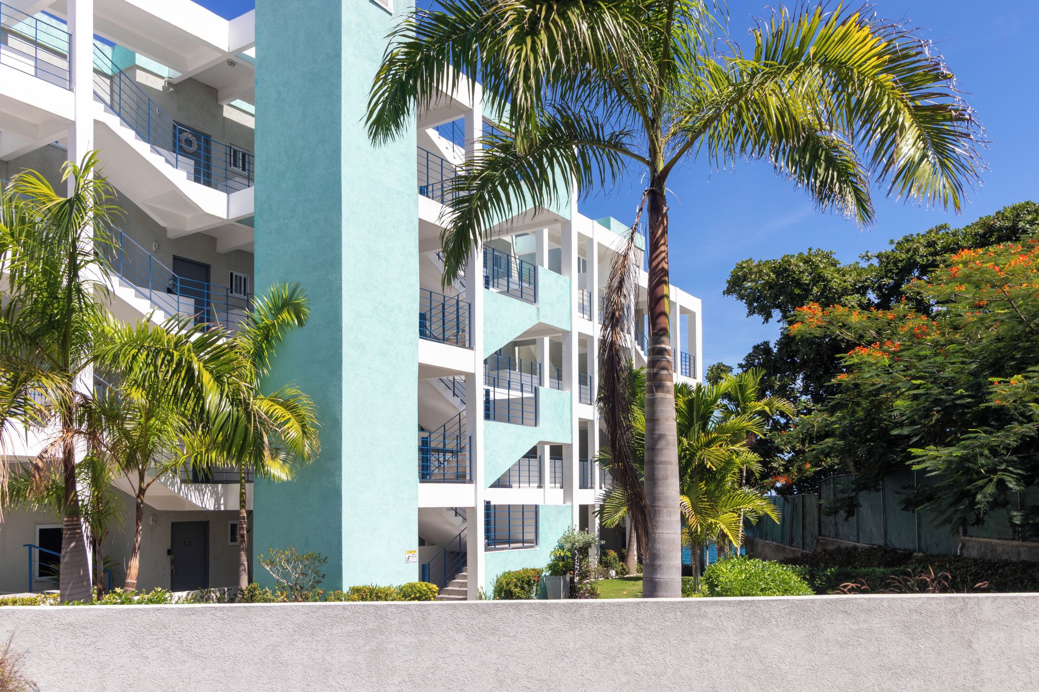 A multi-story building with balconies, palm trees, and a clear blue sky.