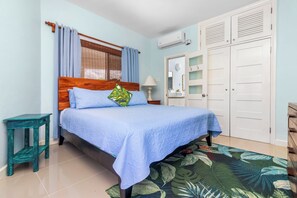 A bedroom with a bed, a nightstand, a wardrobe, and a window with curtains. - Blue Serenity Oceanfront Penthouse (Tower Isle)