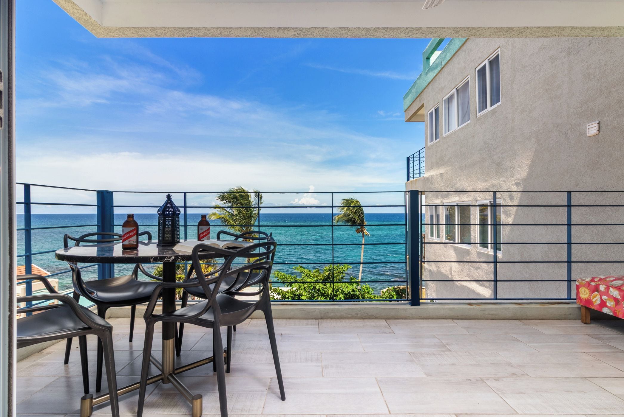 Een balkon met een tafel en stoelen, met uitzicht op de kust, palmbomen en de zee.