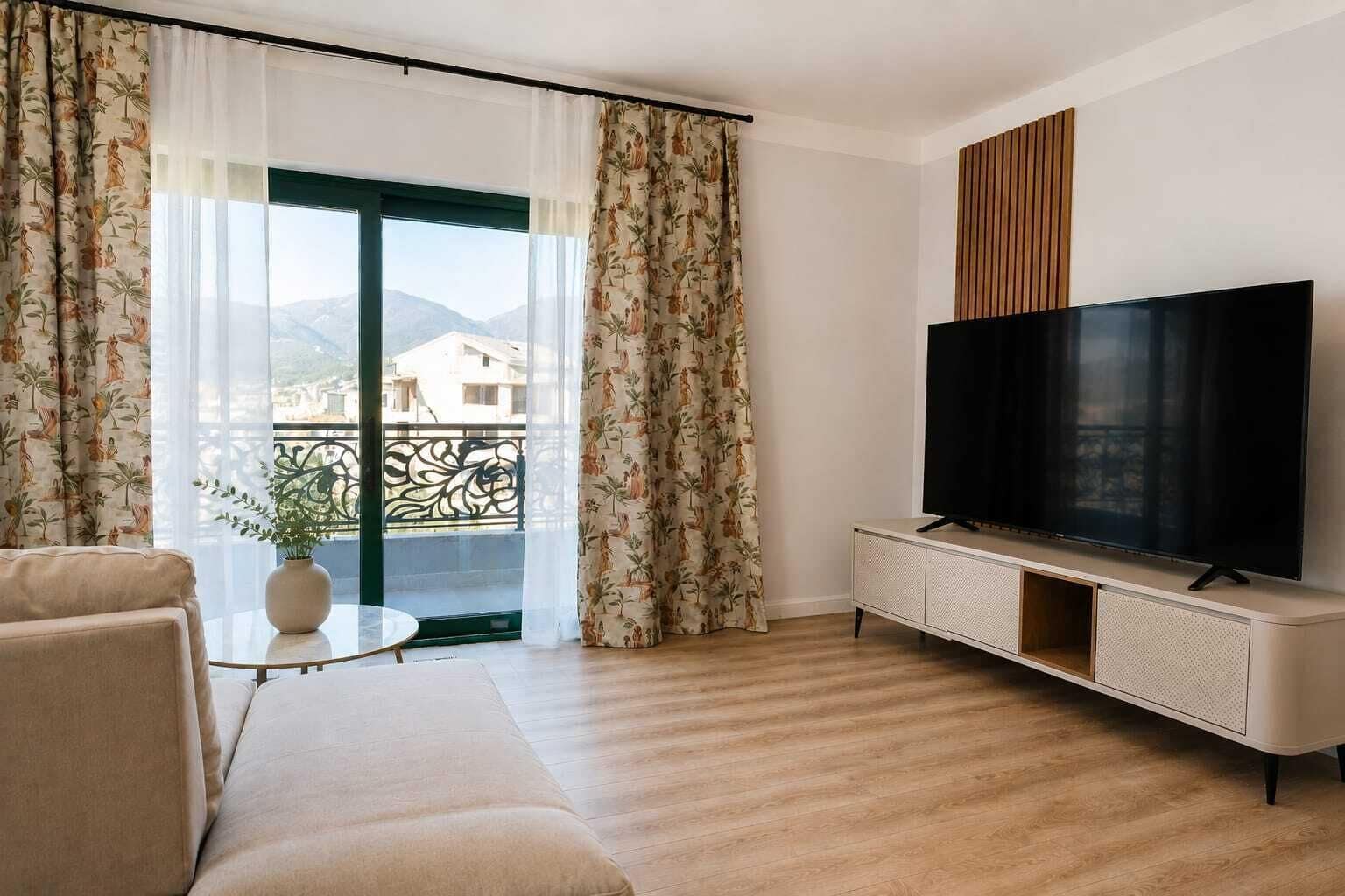 A modern living room with a sofa, a TV on a cabinet, and a balcony with curtains.