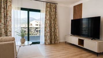 A modern living room with a sofa, a TV on a cabinet, and a balcony with curtains.