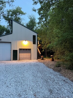 A single-story building with a garage, a small porch with a chair, and a gravel driveway.