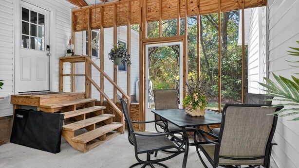 Un patio cubierto con una mesa y sillas de madera, una pequeña escalera y vistas al exterior.