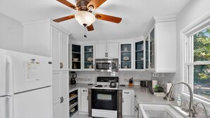 Una cocina con armarios blancos, estufa, horno, microondas y ventilador de techo.