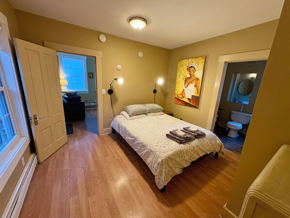 Un dormitorio con cama, un cuadro, un baño y una puerta que da a otra habitación.