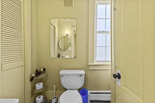 A bathroom with a toilet, a mirror, a window, and a heater.
