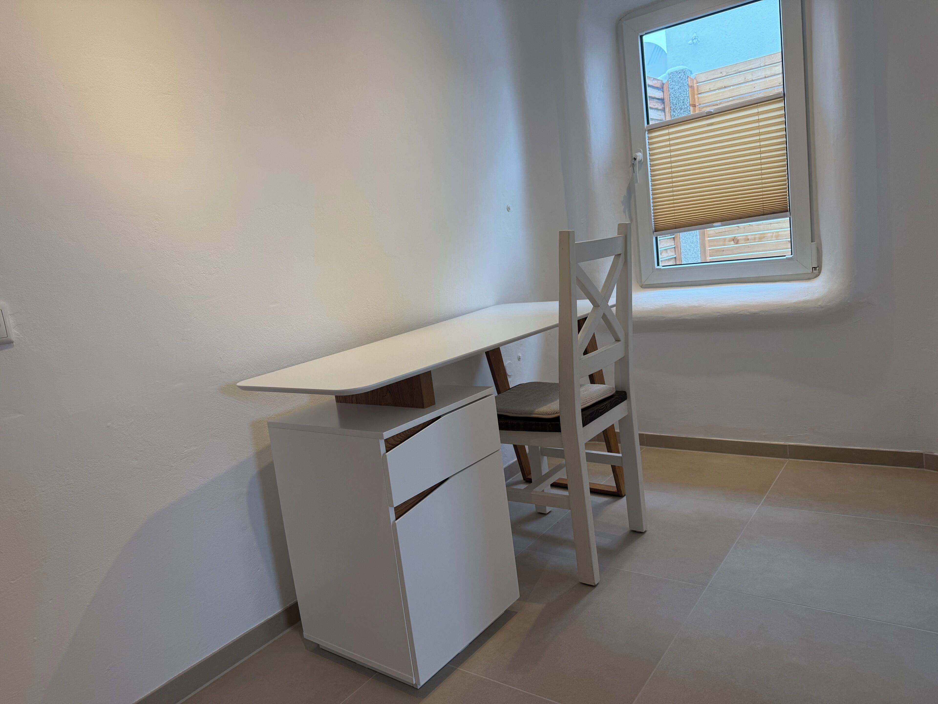 A corner room with a white desk, chair, and built-in storage unit.