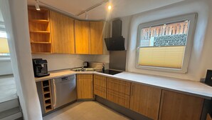 Une cuisine moderne avec des meubles en bois, un lave-vaisselle encastré, une machine à café et une fenêtre avec des stores.