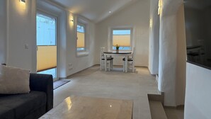 Un intérieur moderne comprenant un canapé, une table basse, un coin repas avec une table et des chaises, et un escalier.