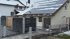 Un bâtiment dont le toit est recouvert de neige, avec une porte en métal et une enseigne sur laquelle on peut lire « Herzlich Willkommen ».
