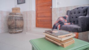 A green table with a stack of books, a wooden barrel, and a dark armchair with a plaid blanket.