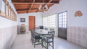 A dining area with a wooden table and chairs, a chandelier, a wooden door, and a window with curtains.