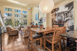 A spacious living area with a wooden dining table, comfortable seating, large windows, and a painting on the wall. - Pool, Hot Tub, 3 bedrooms 3 bathrooms walkable cute neighborhood near downtown. (Houston)