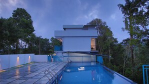 Une maison moderne dotée d’une piscine, d’un balcon et offrant une vue sur les arbres environnants.