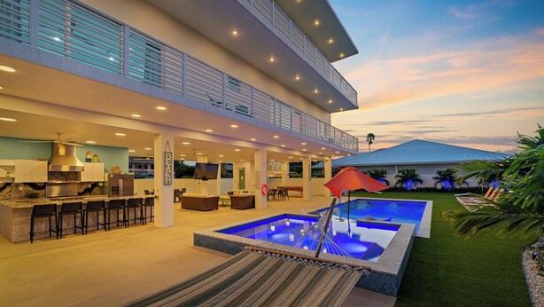 Un espace cuisine extérieur moderne, doté d’une piscine, d’un hamac et d’un coin salon abrité.