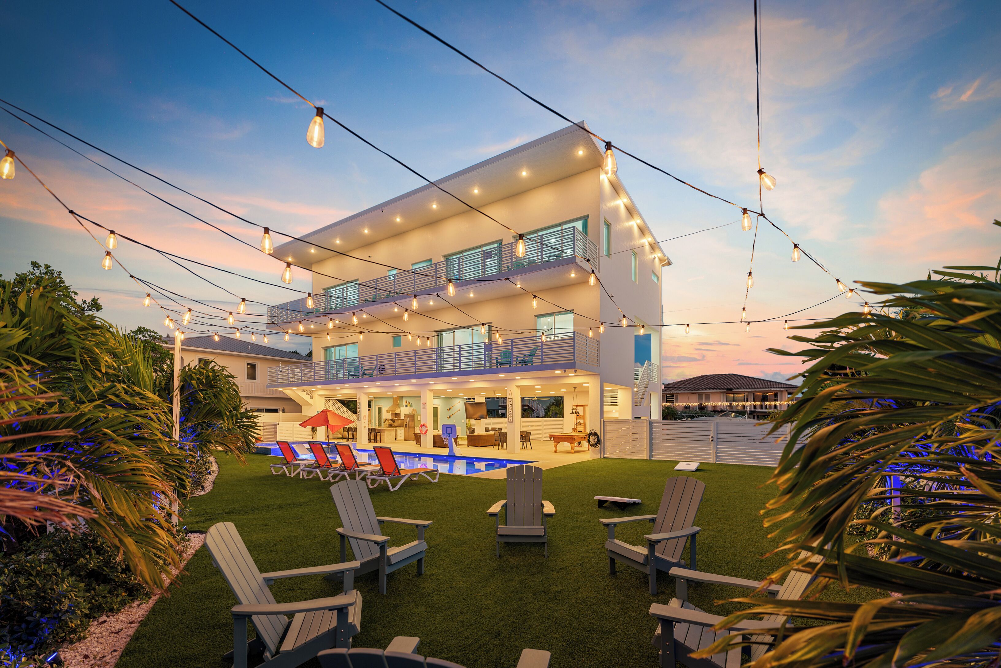 A two-story building with a pool area, outdoor seating, and string lights.