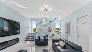 Un salon moderne avec une cheminée, des canapés en cuir noir, un grand téléviseur et un escalier menant à un autre niveau.