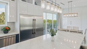 Une cuisine moderne dotée d’un réfrigérateur en acier inoxydable, d’un plan de travail en marbre et d’un luminaire suspendu.