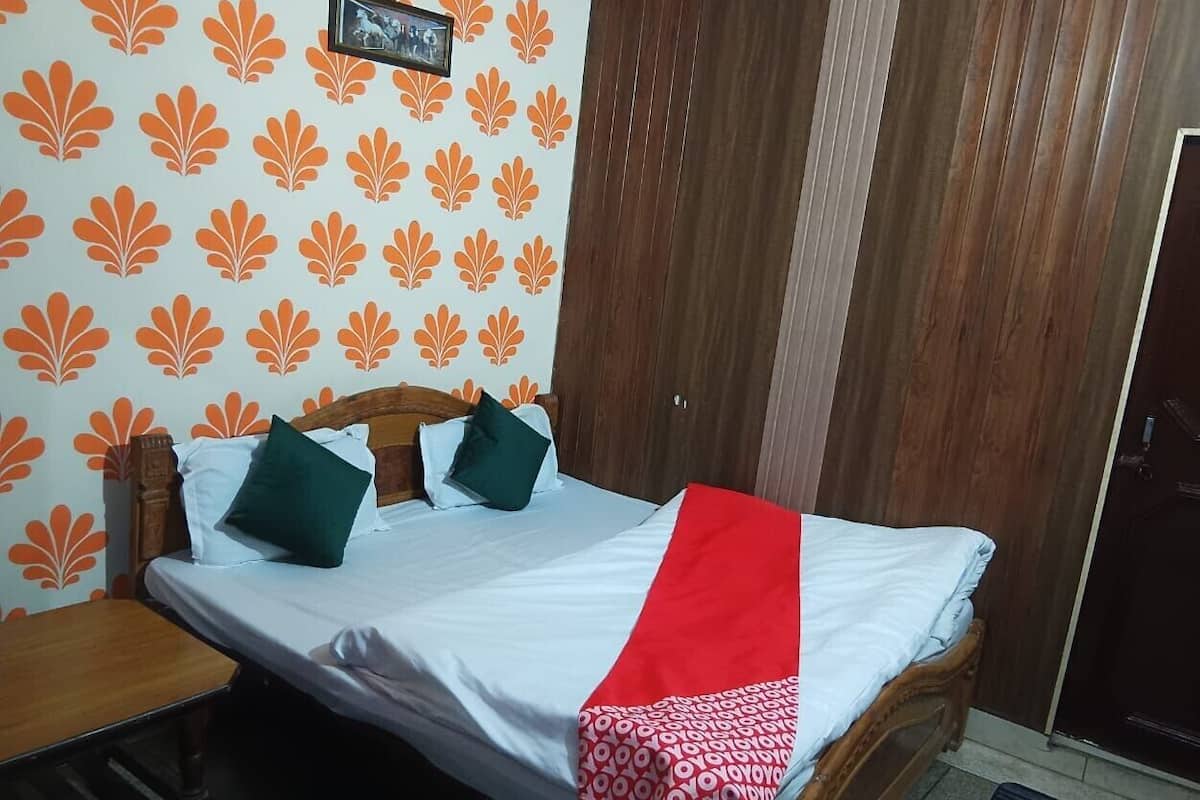 A single bed with a wooden headboard, white bedding, and a red and white patterned throw.