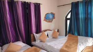 Quarto com duas camas, cortinas roxas, cabeceira de madeira e um objeto decorativo na parede.