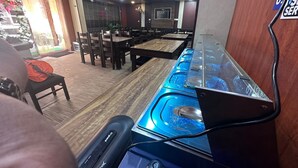Um restaurante com mesas e cadeiras de madeira, área de buffet com copos de vidro azul e um letreiro indicando uma área de serviço.