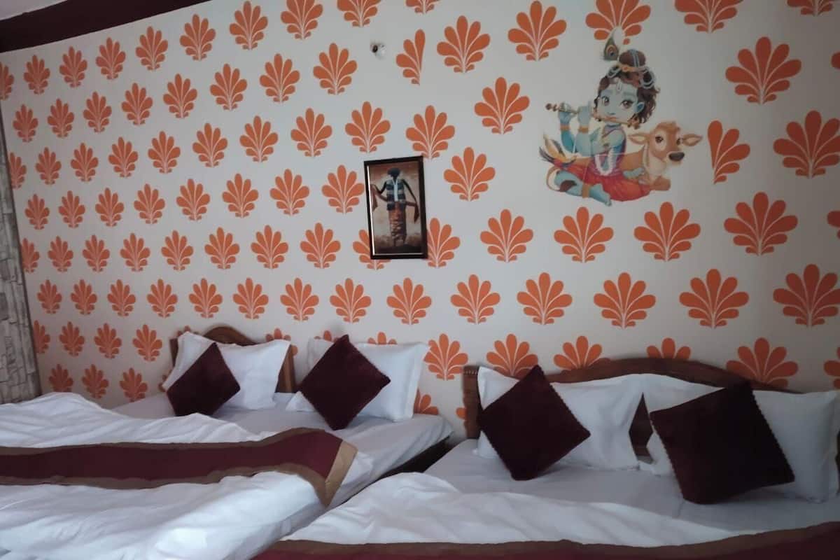 A hotel room with a patterned wall, a bed with white bedding and brown pillows, and a framed picture of a deity.