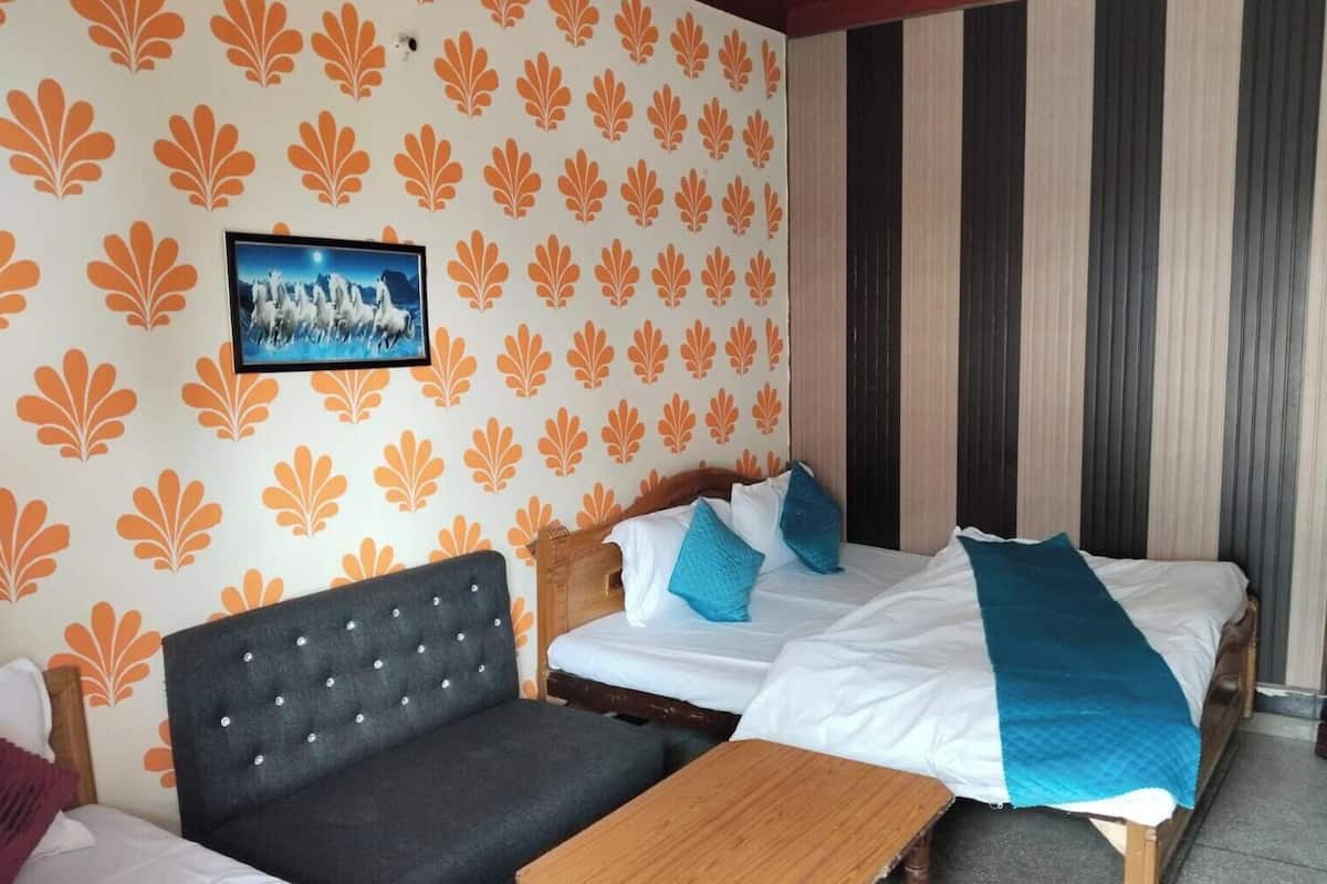 A hotel room with a bed, a sofa, a wooden table, and a wall with a leaf pattern.