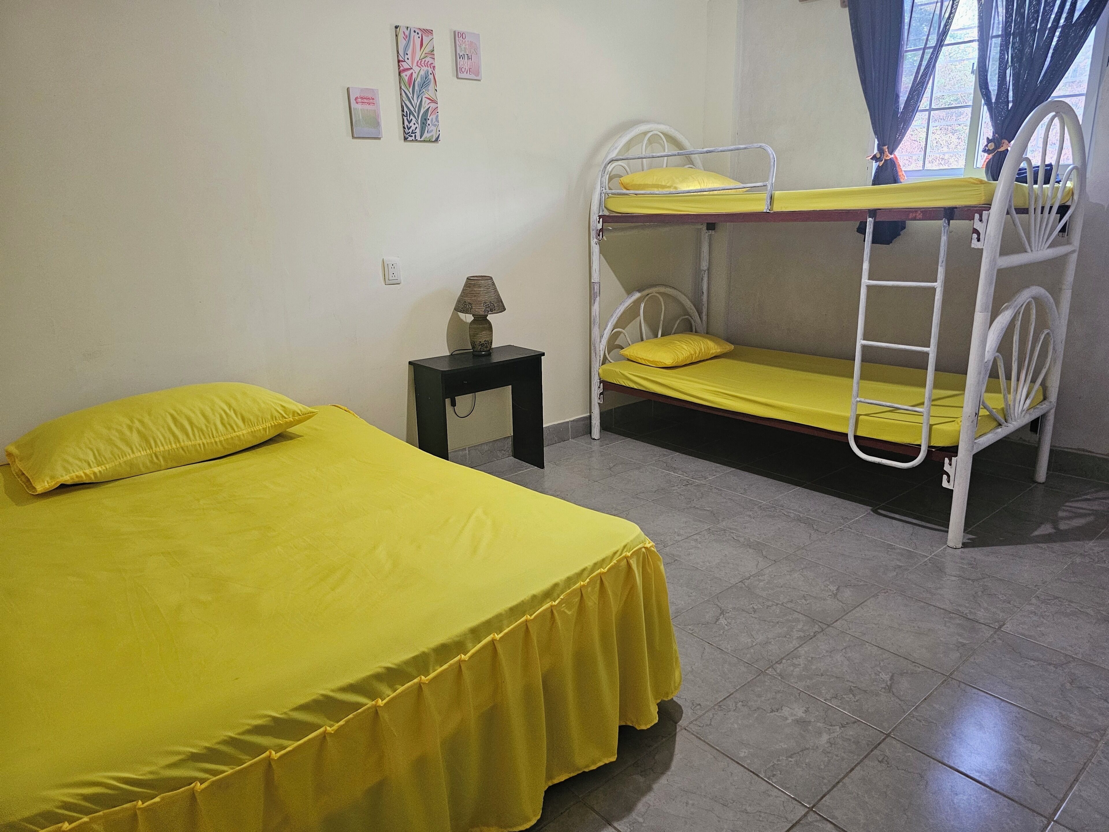 A room with a single bed, a bunk bed, a nightstand with a lamp, and a window with curtains.