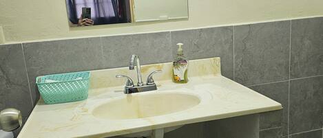 A bathroom with a sink, mirror, and a window above it.