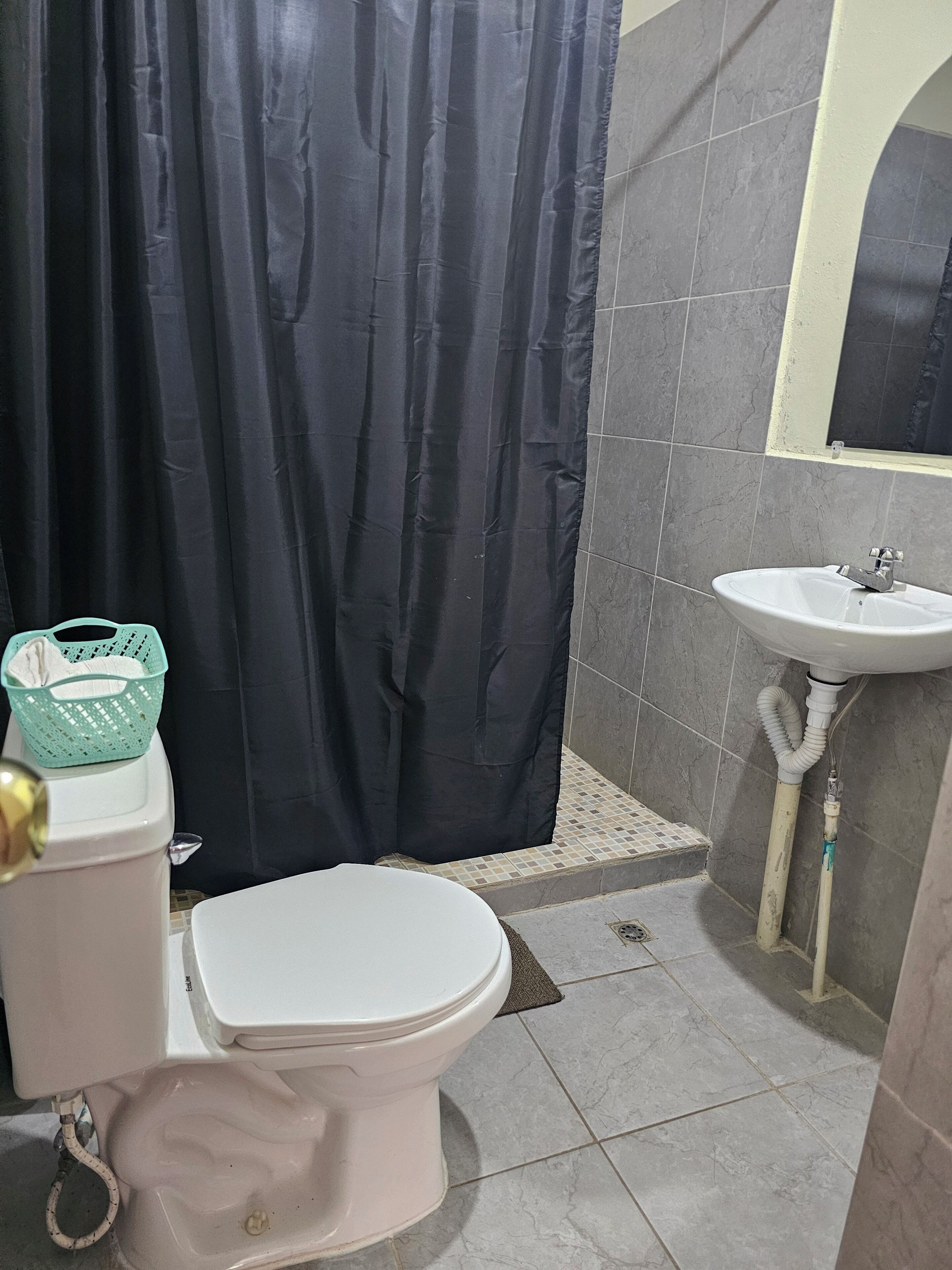 A bathroom with a toilet, a sink, a shower curtain, and a tiled floor.