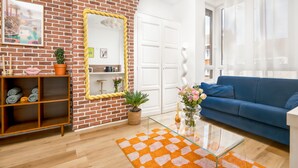 A living room with a brick wall, a blue sofa, a glass coffee table, and a wooden shelf with towels. - Palm Springs - Studio Design & Lumineux in Malo Proche Plage (Dunkerque)