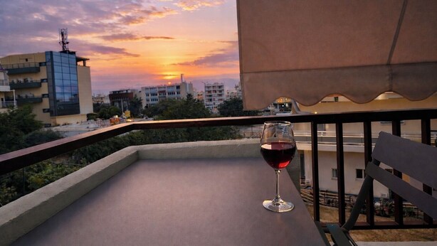 Ein Balkon mit einem Glas Rotwein, Blick auf Gebäude und Sonnenuntergang.