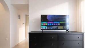 Ein modernes Zimmer mit einem Flachbildfernseher auf einer schwarzen Kommode, einem Flur mit einer Tür und einem Lichtschalter an der Wand.