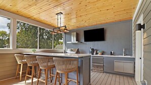 A modern kitchen with a wooden ceiling, large windows, a flat-screen TV, and a bar area with wicker chairs. - NEW LUXURY Condo - Walk to The Abbey! Sleeps 10! Fontana-on-Geneva Lake (Fontana-on-Geneva Lake)