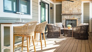 A covered outdoor seating area with wicker furniture, a stone fireplace, and a ceiling fan. - NEW LUXURY Condo - Walk to The Abbey! Sleeps 10! Fontana-on-Geneva Lake (Fontana-on-Geneva Lake)