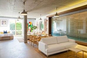 Un salon moderne avec un canapé blanc, une table à manger et des chaises, de grandes fenêtres et une cloison en verre.