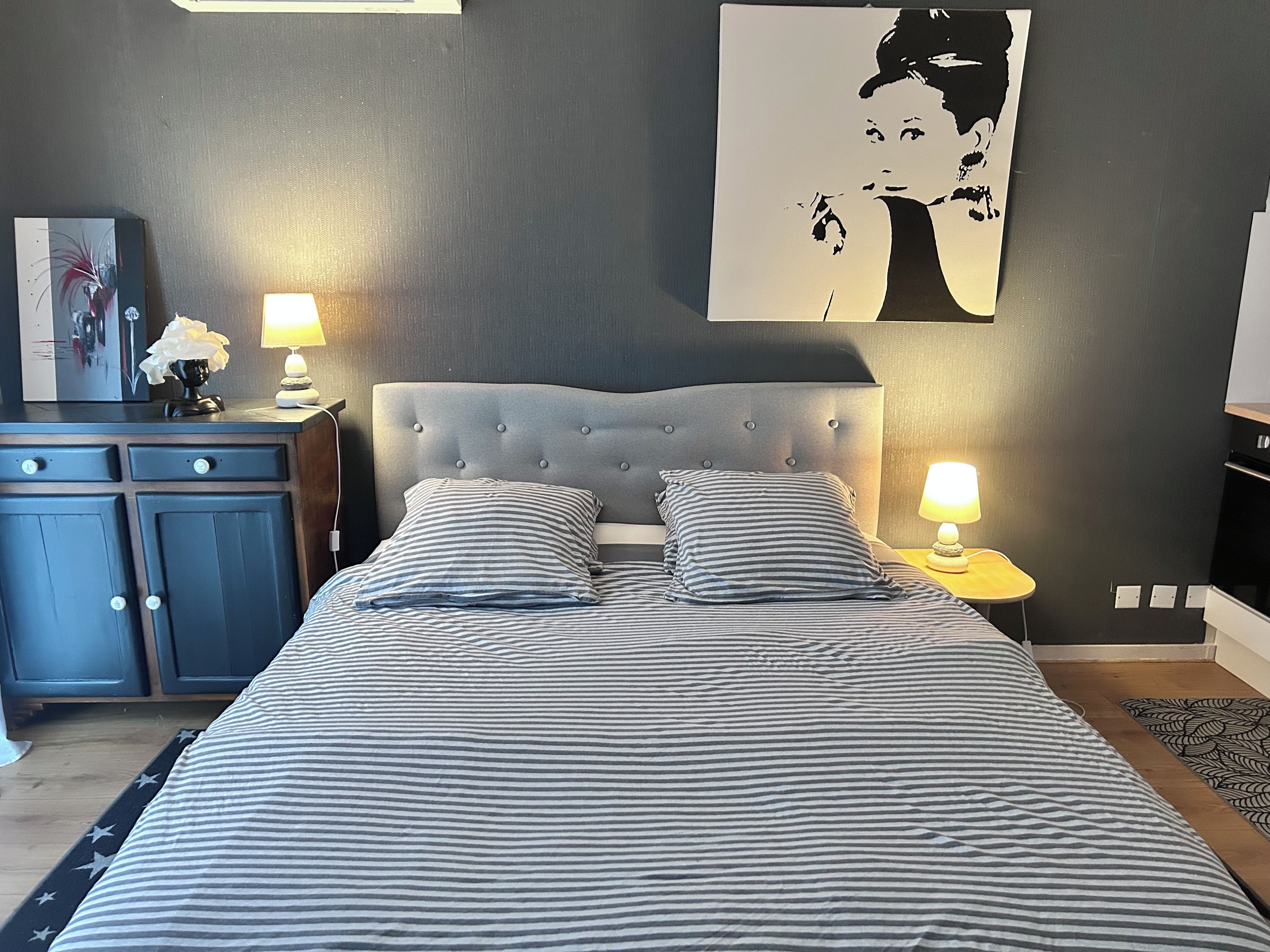A bedroom with a bed, two bedside lamps, a dresser, and a wall-mounted painting.