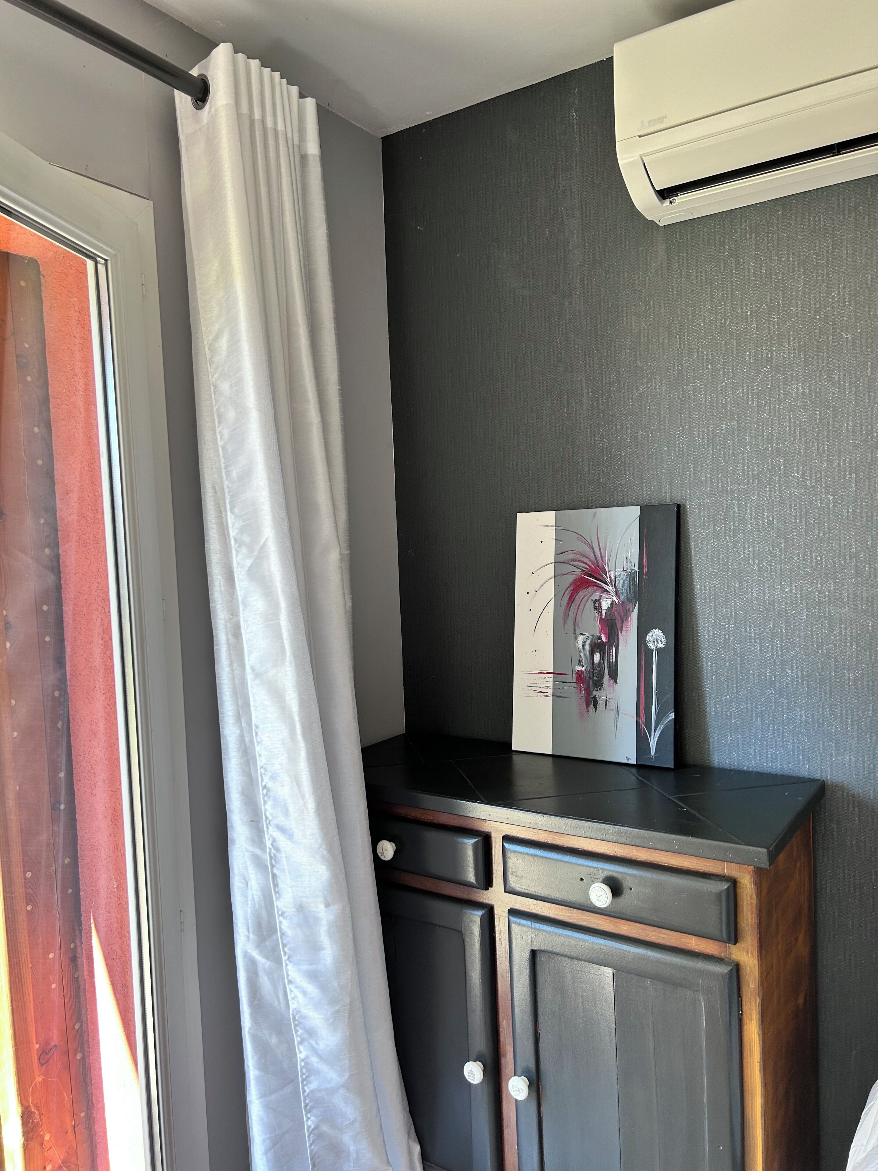 A room with a sliding door, a white curtain, a black cabinet with drawers, and a wall-mounted air conditioner.