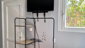 Huoneessa on seinälle asennettu televisio, puinen hyllykkö, ovi ja ikkuna, josta on näkymä vehreään maisemaan.