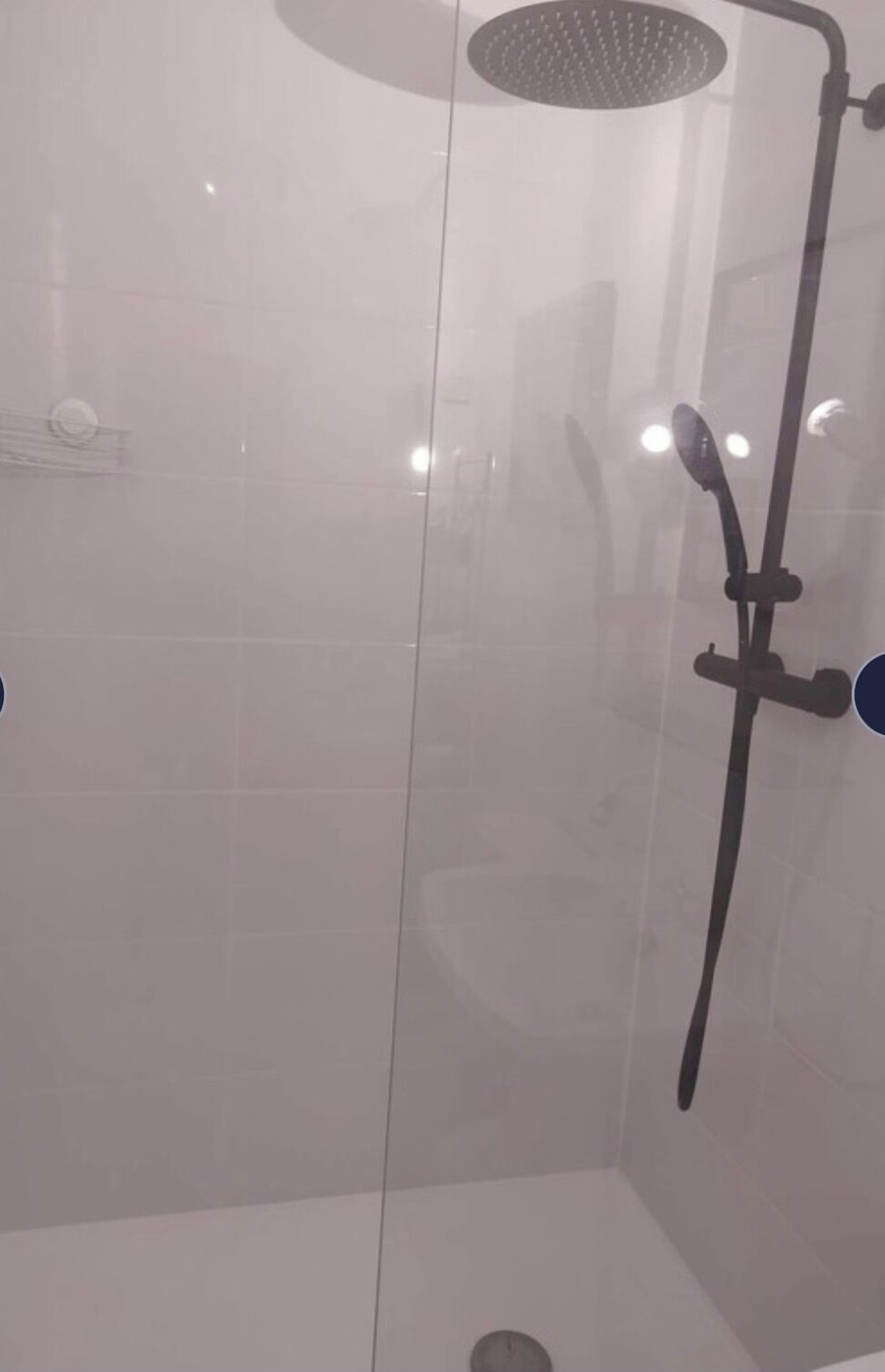 Un área de ducha con paredes de vidrio, un cabezal de ducha de mano y un grifo instalado en la pared.