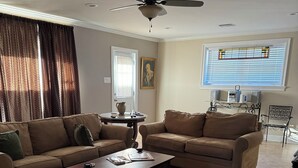 A living room with a sectional sofa, a coffee table, a ceiling fan, a window with blinds, and a decorative rug. - Lovely Furnished Vintage Home (New Orleans)