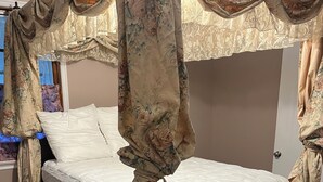 A bedroom with a canopy bed, wooden flooring, and a window with curtains. - Lovely Furnished Vintage Home (New Orleans)