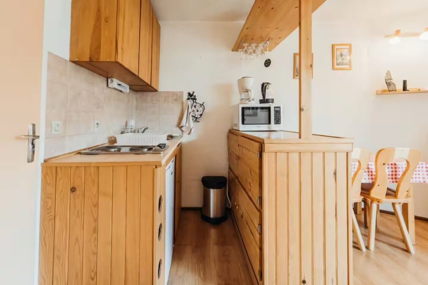 A compact kitchen with wooden cabinets, a microwave, a coffee maker, and a trash bin.