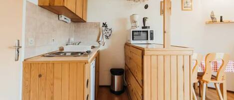A compact kitchen with wooden cabinets, a microwave, a coffee maker, and a trash bin.