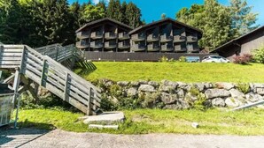 Un edificio a più piani con balconi, un muro di sostegno in pietra e una scala in legno che conduce a una zona erbosa.
