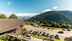Un parcheggio con auto, un edificio con tetto spiovente e un paesaggio montuoso sullo sfondo.