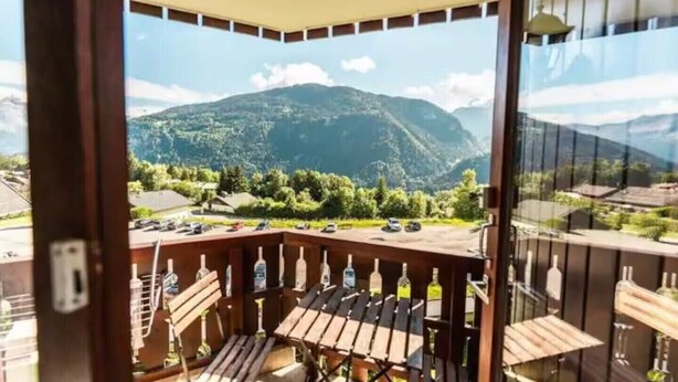 Un balcone con vista su una montagna, un tavolo e diverse bottiglie.